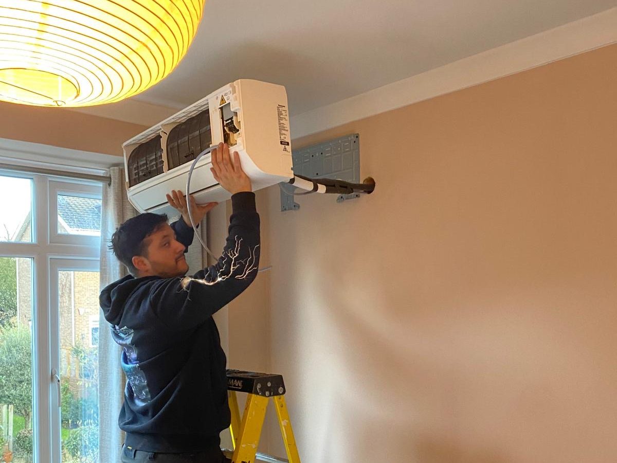 Fitter mounting a wall split unit onto its bracket in a bedroom