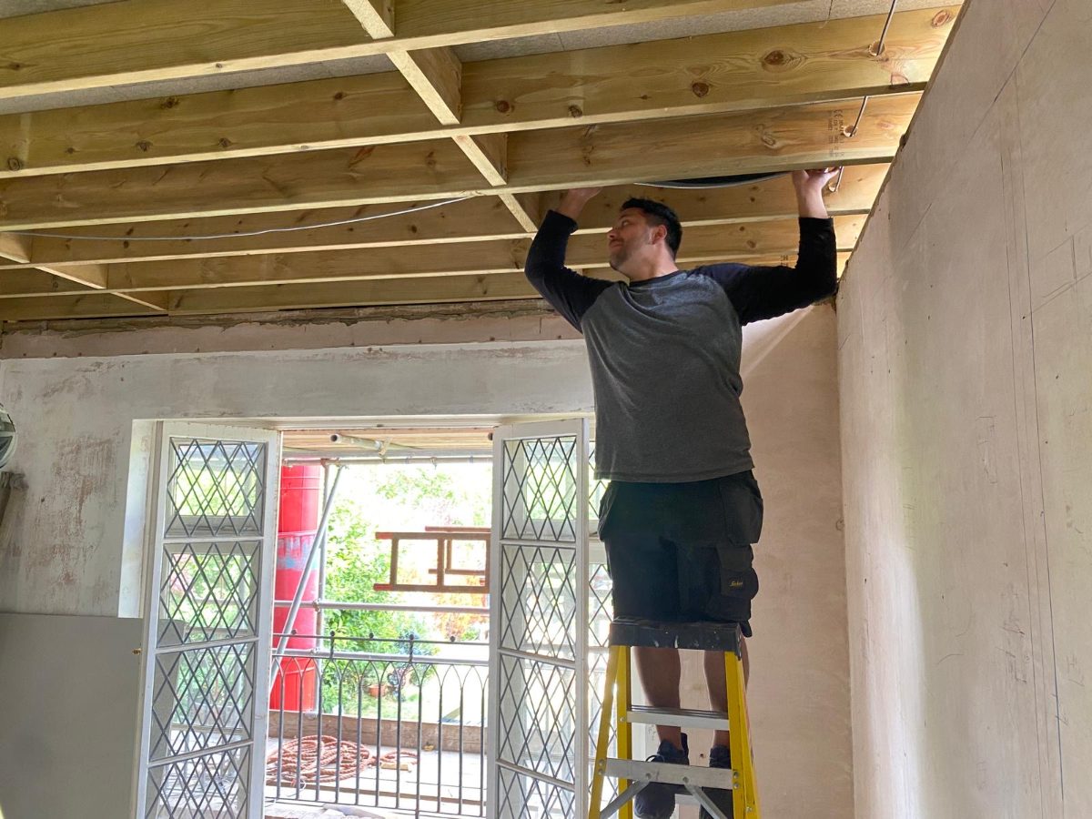 Fitter on a step ladder pushing pre-insulated pipe above new ceiling joists
