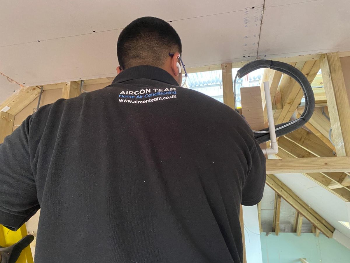 Close-up of an Aircon Team fitter feeding pre-insulated pipe through roof timbers