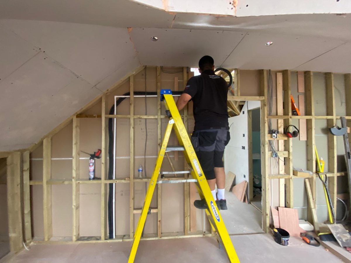 Fitter on a ladder running pre-insulated pipe through the timber studwork of a loft conversion