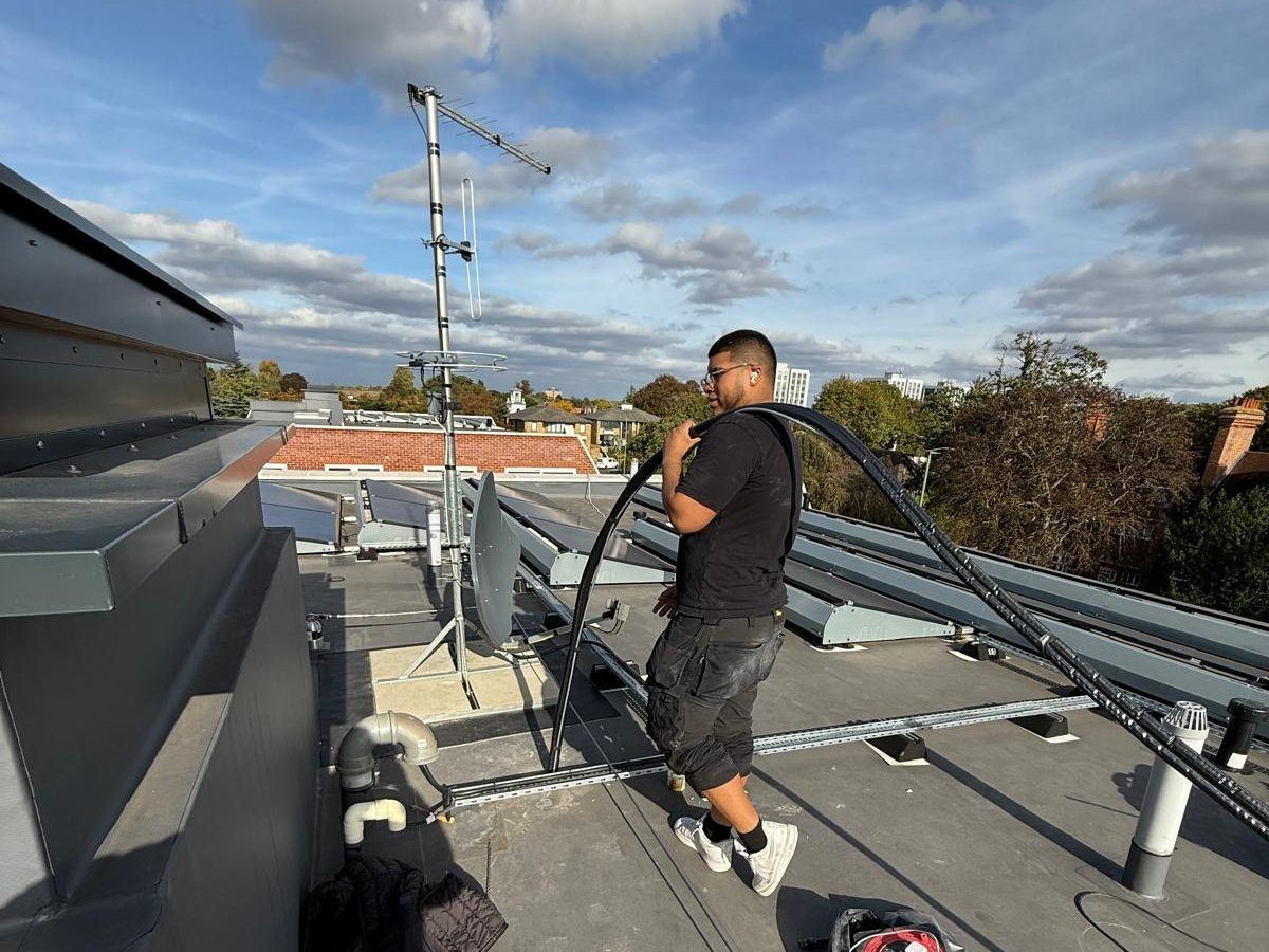 Fitter carrying a coil of pre-insulated pipe across a flat roof past rooftop plant